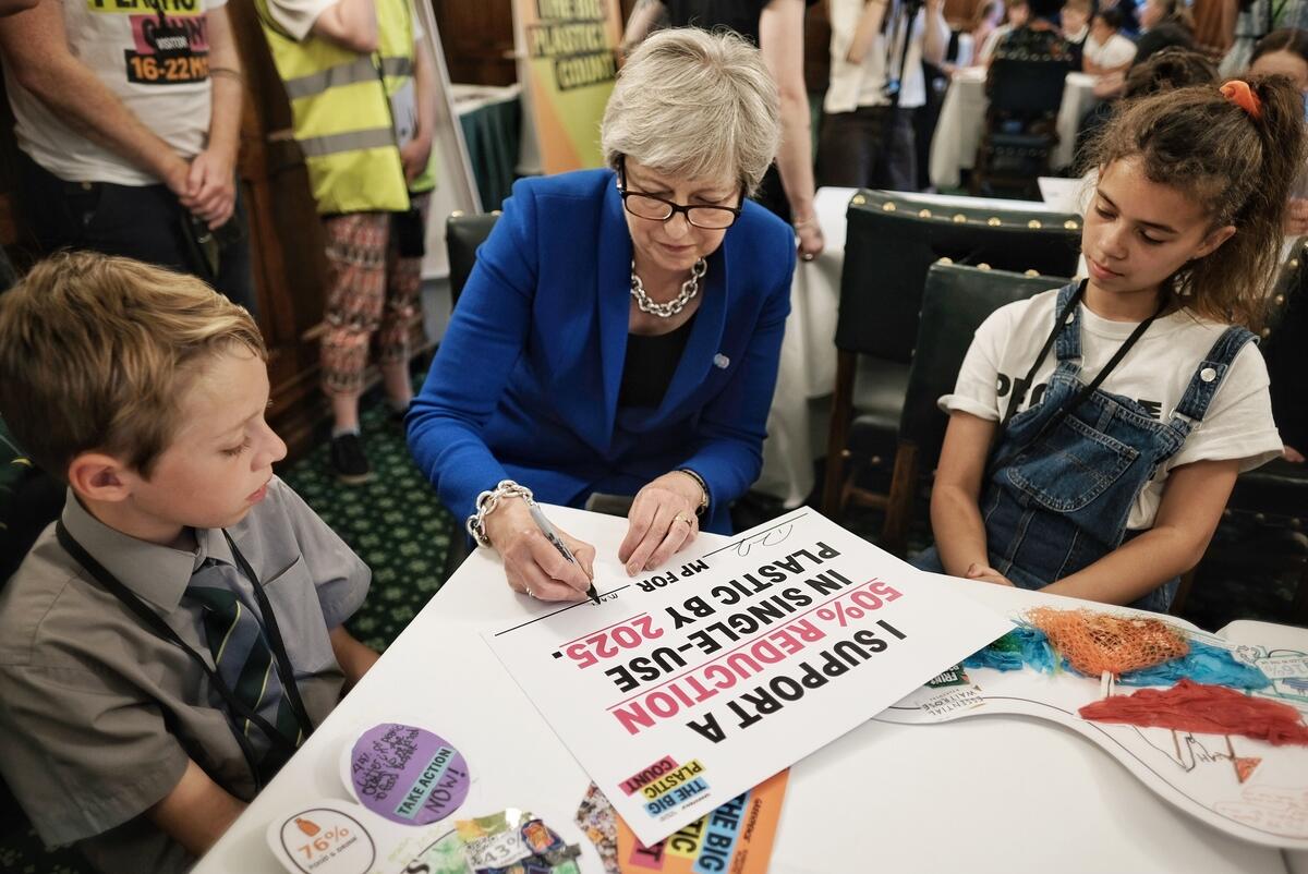 Theresa May sat with two school pupils signing a pledge to support a 50% reduction in single-use plastic by 2025.