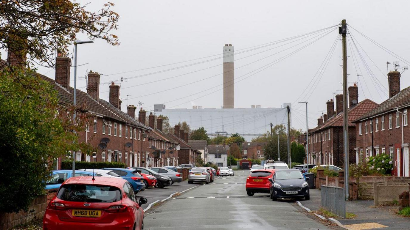 Rows of terraced houses line a street in England which is overlooked by a large waste incineration facility