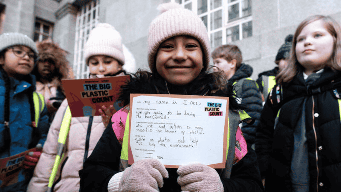 Primary school pupils wearing winter gear hold pledge cards outside a government building