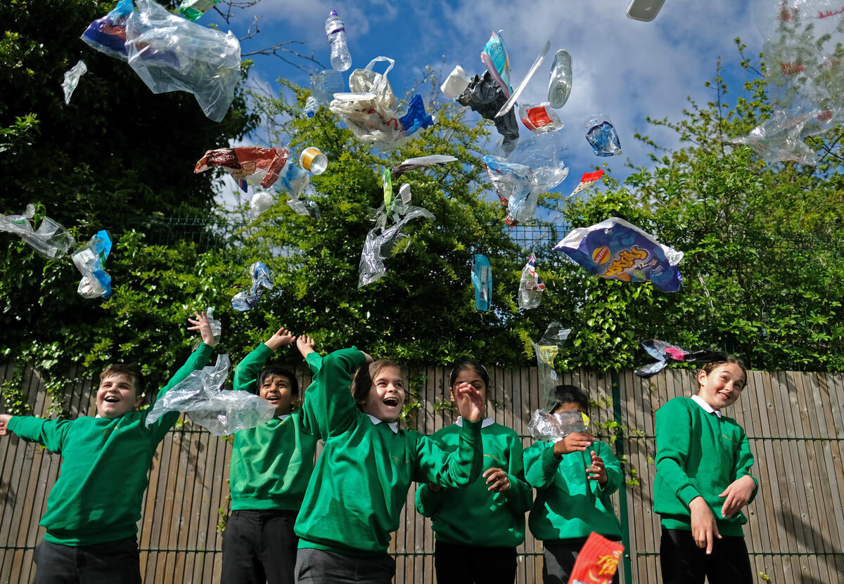 Primary school pupils joyfully throwing pieces of plastic packaging into the air