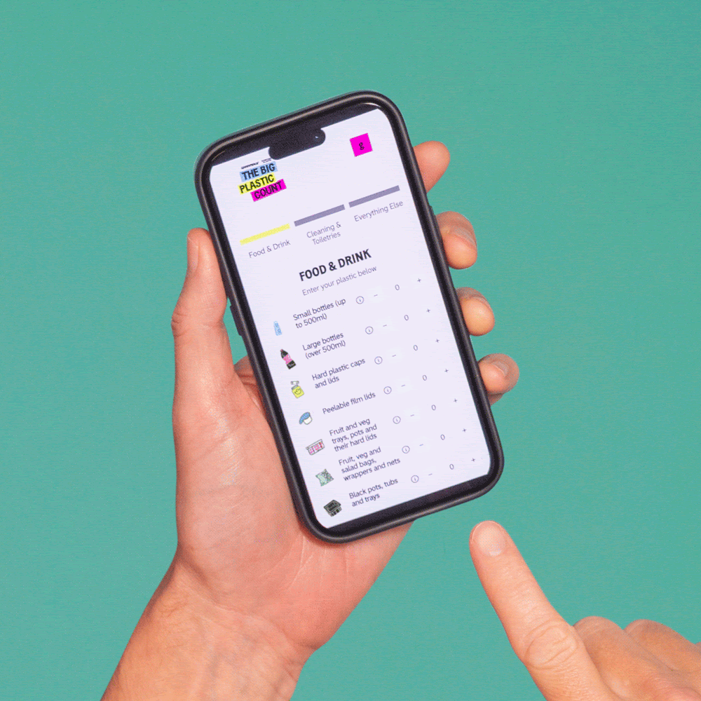 A hand holds a phone, while the other points to The Big Plastic Count app